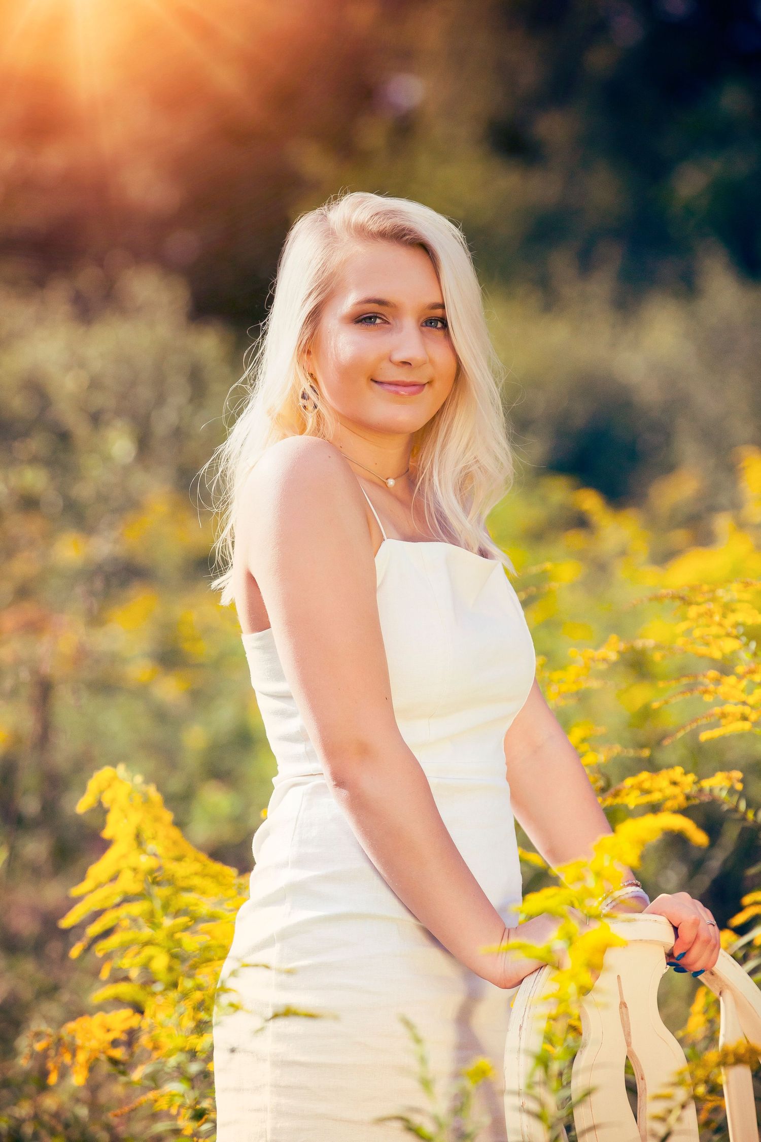 Beautiful outdoor portrait in a white dress surrounded by vibrant yellow wildflowers in warm sunlight.