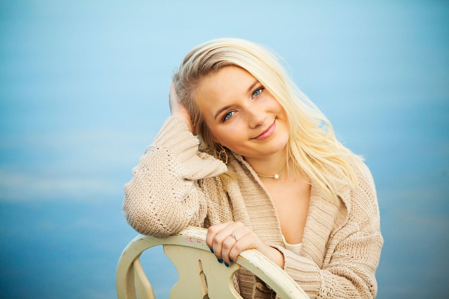 Cozy portrait against blue sky wearing a beige sweater with a gentle smile.