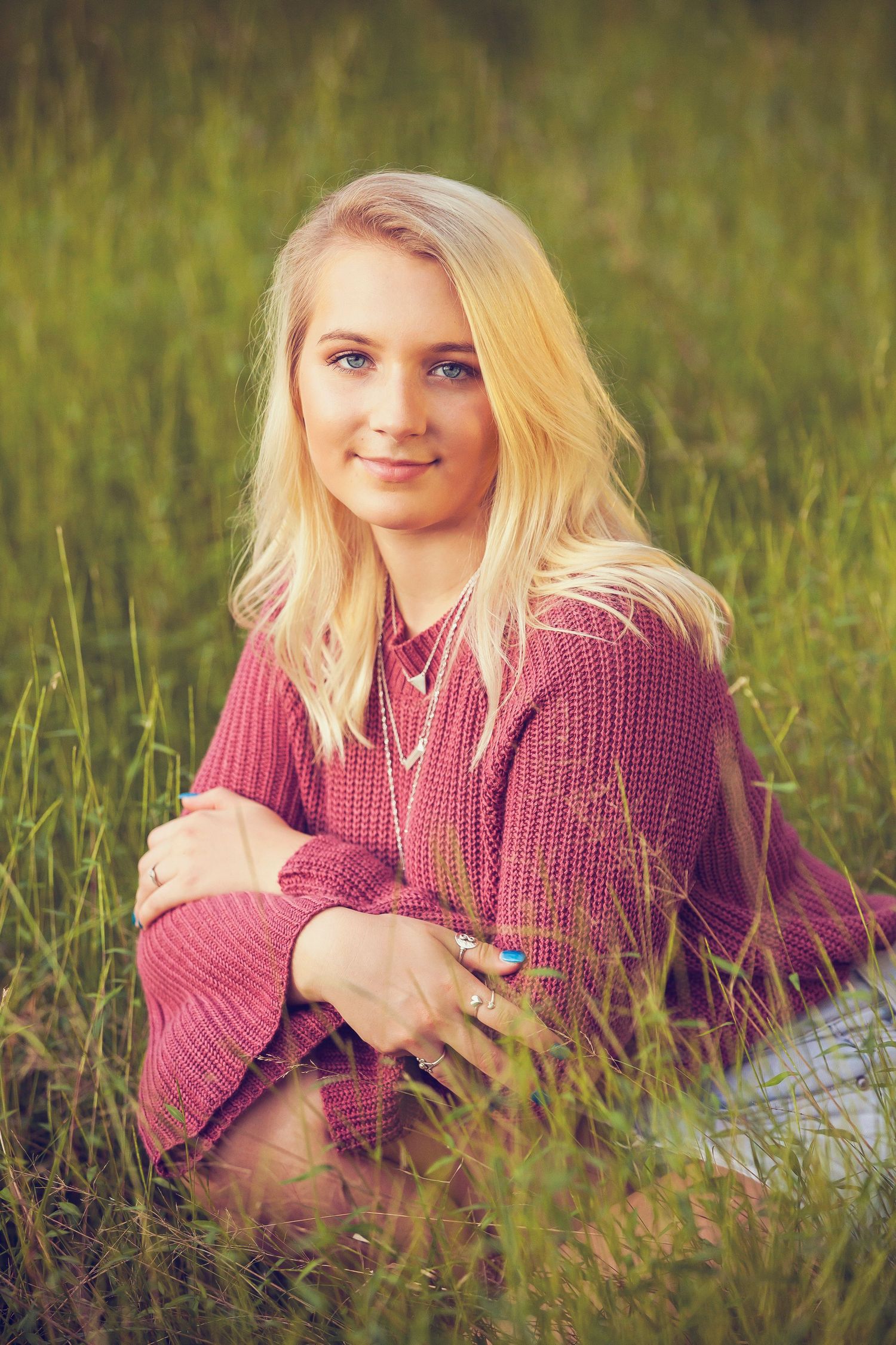 Casual outdoor portrait in a burgundy sweater sitting in tall grass during golden hour.