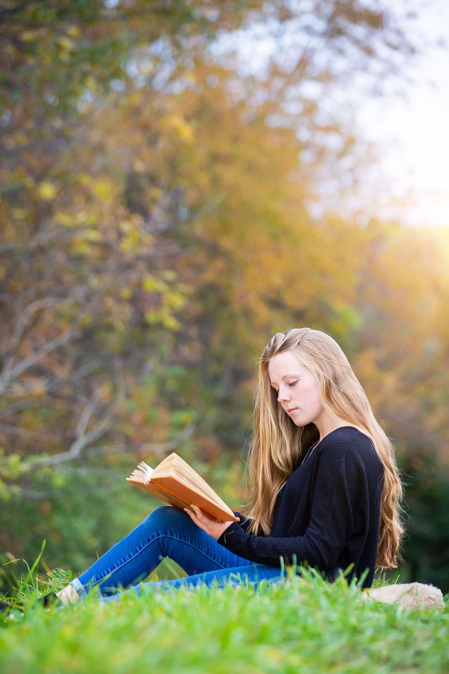 Person reading a book while sitting on grass during golden hour in autumn.