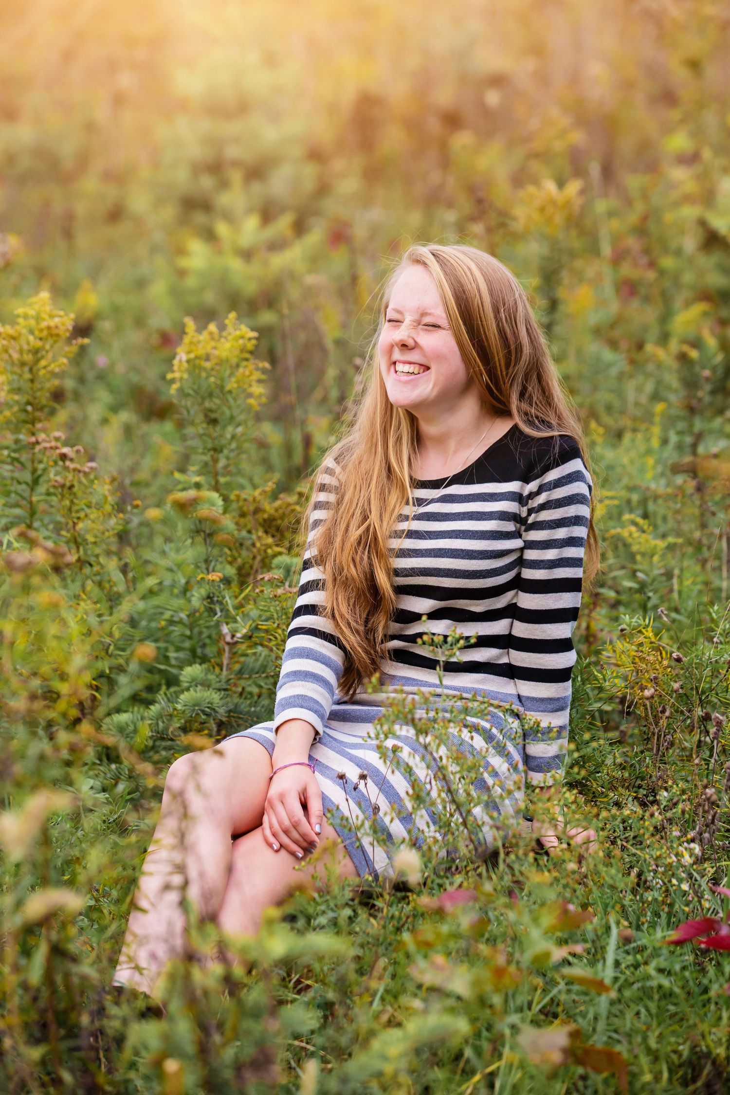 Portrait of someone sitting in a wildflower field wearing a striped top during golden hour.