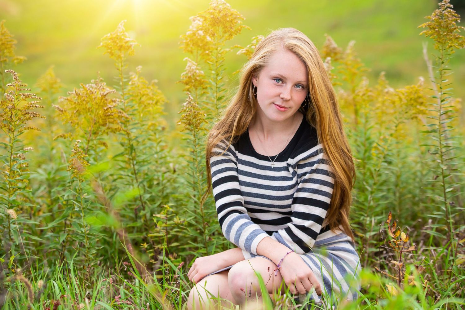 Person in striped sweater sitting among yellow wildflowers in a sunny meadow.