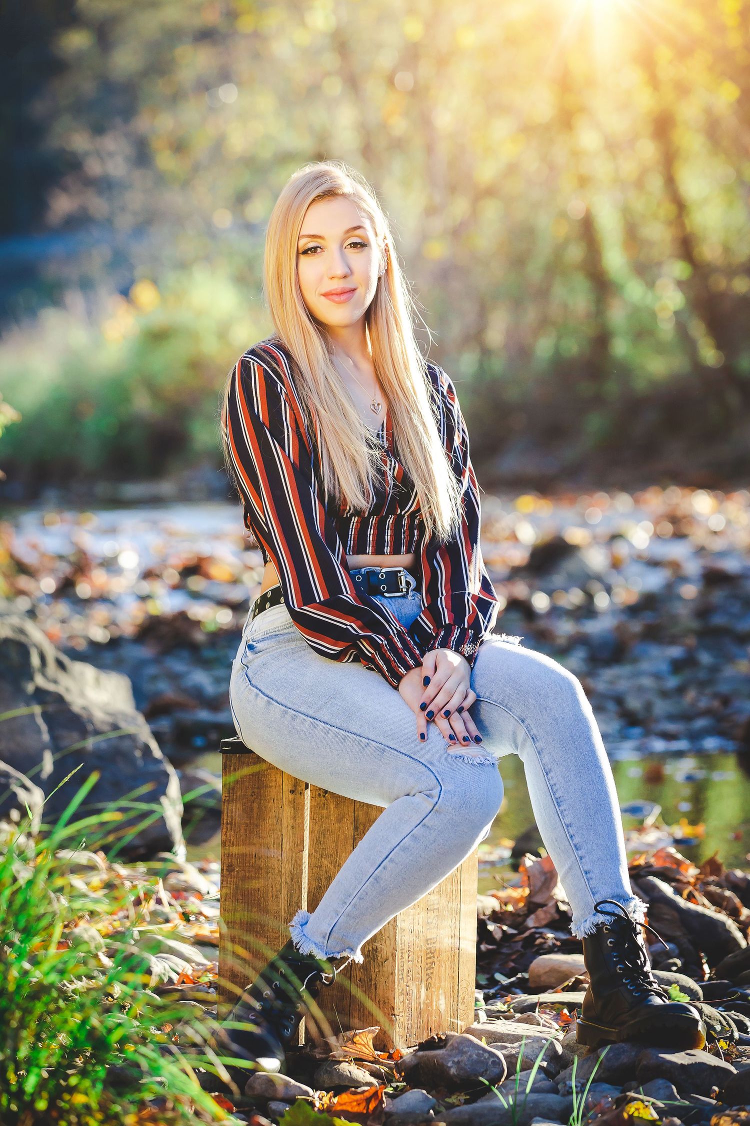 Casual portrait sitting on wooden stump by stream wearing striped top and jeans.