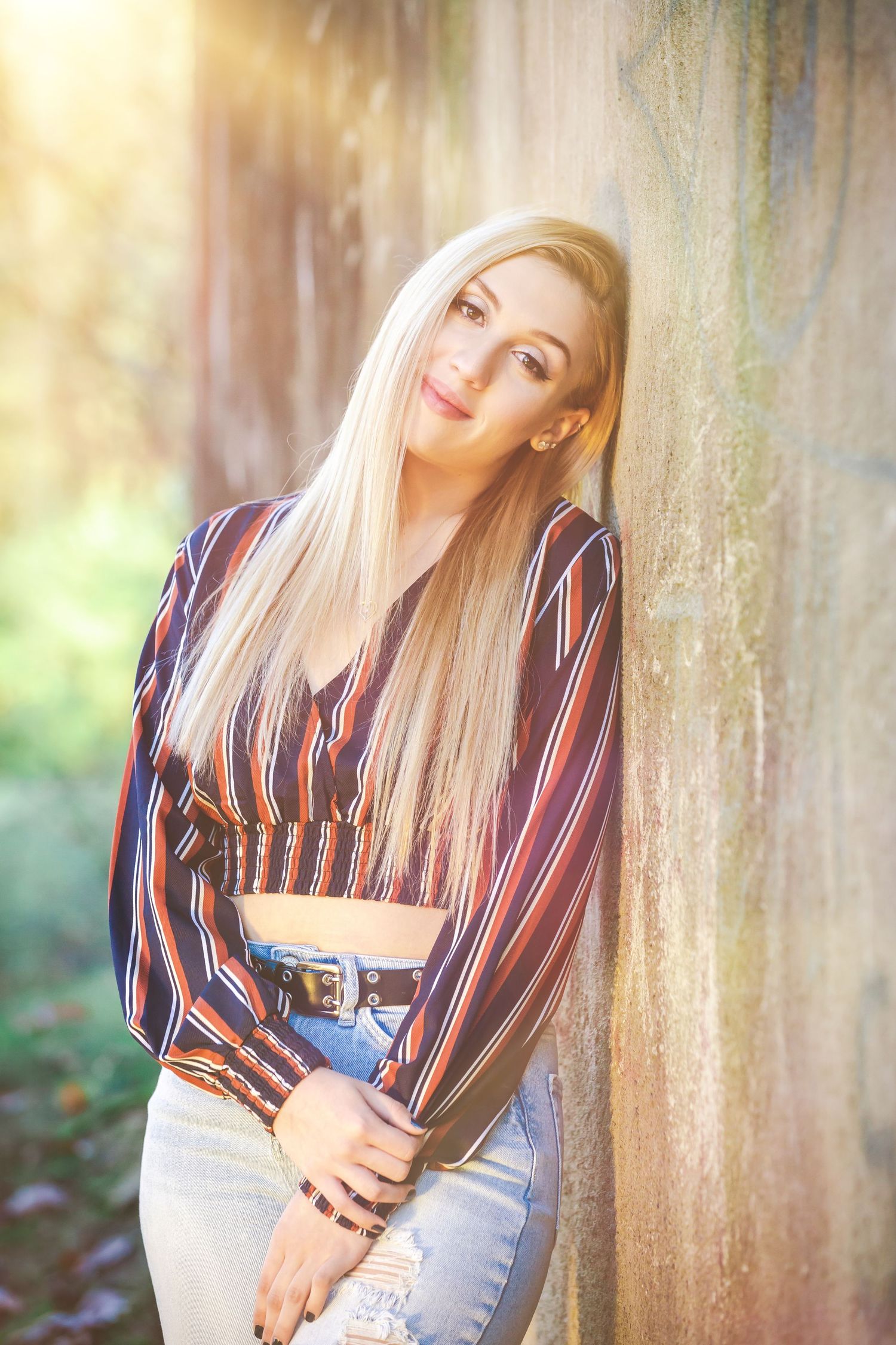 Casual portrait against wall wearing striped crop top and light jeans in warm lighting.
