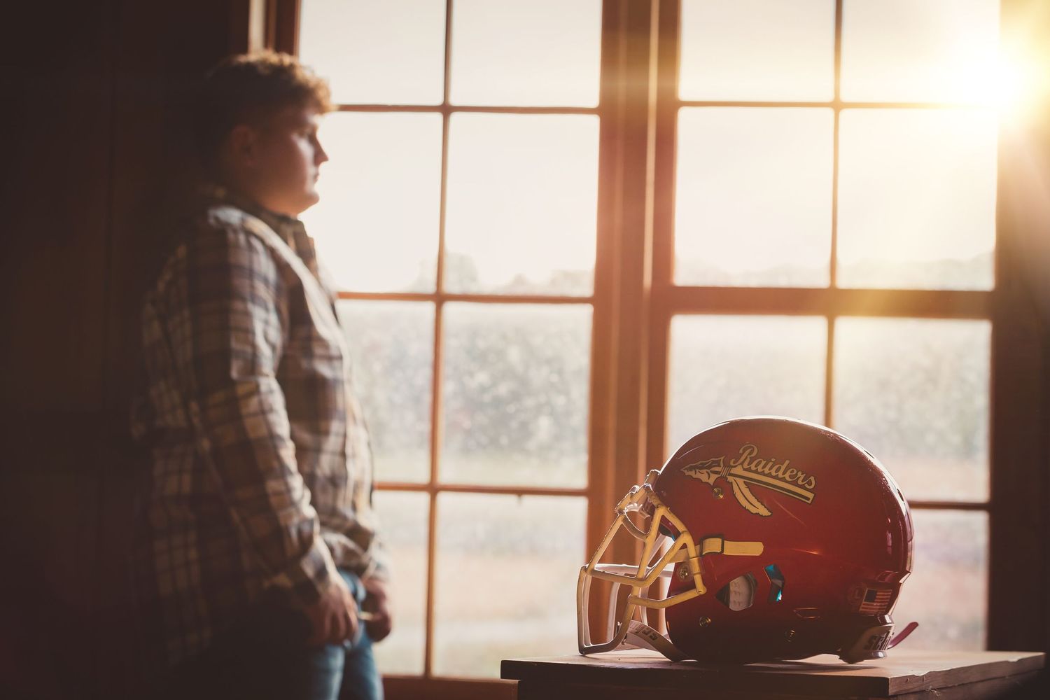 Person looking out window at sunset with football helmet on display.