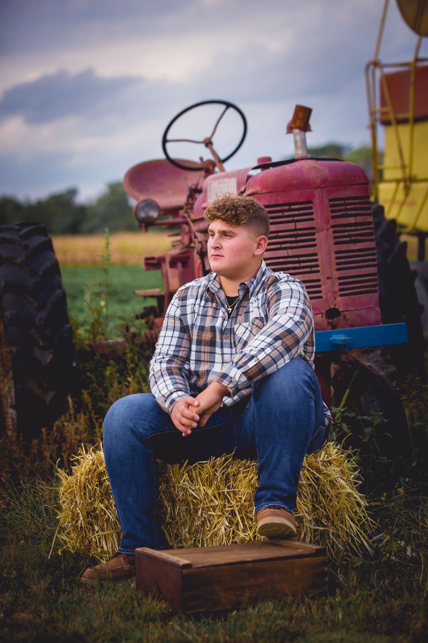 Portrait of person in plaid shirt sitting on vintage red tractor in rural setting.