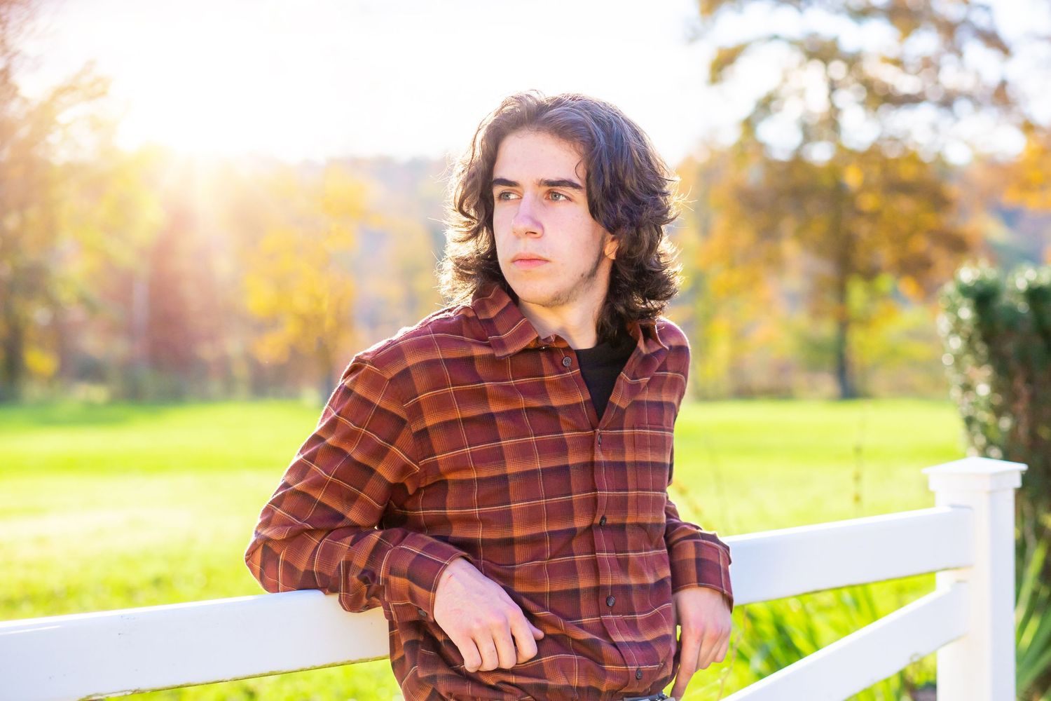 Autumn outdoor portrait featuring a plaid flannel shirt against a sunlit background with white fence.