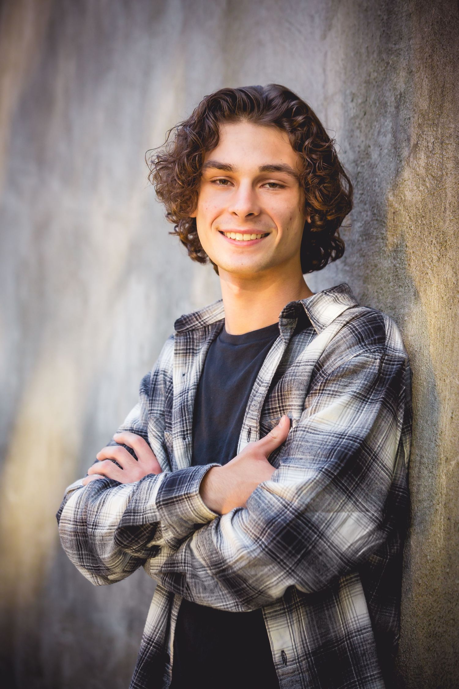 Casual portrait of person in plaid flannel against textured wall with natural lighting.
