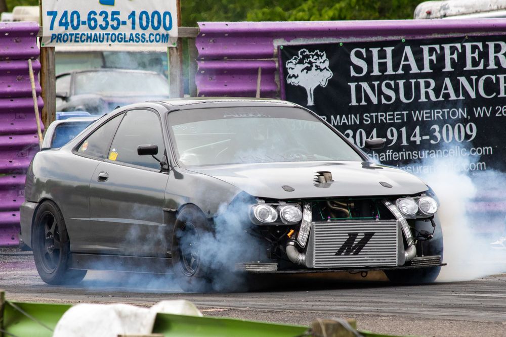 Grey Acura Integra doing a burnout at start of dragstrip