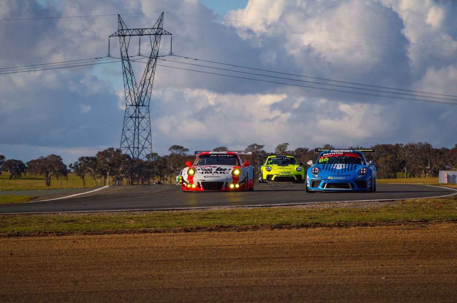 Colorful race cars competing on a track with power lines in the background.