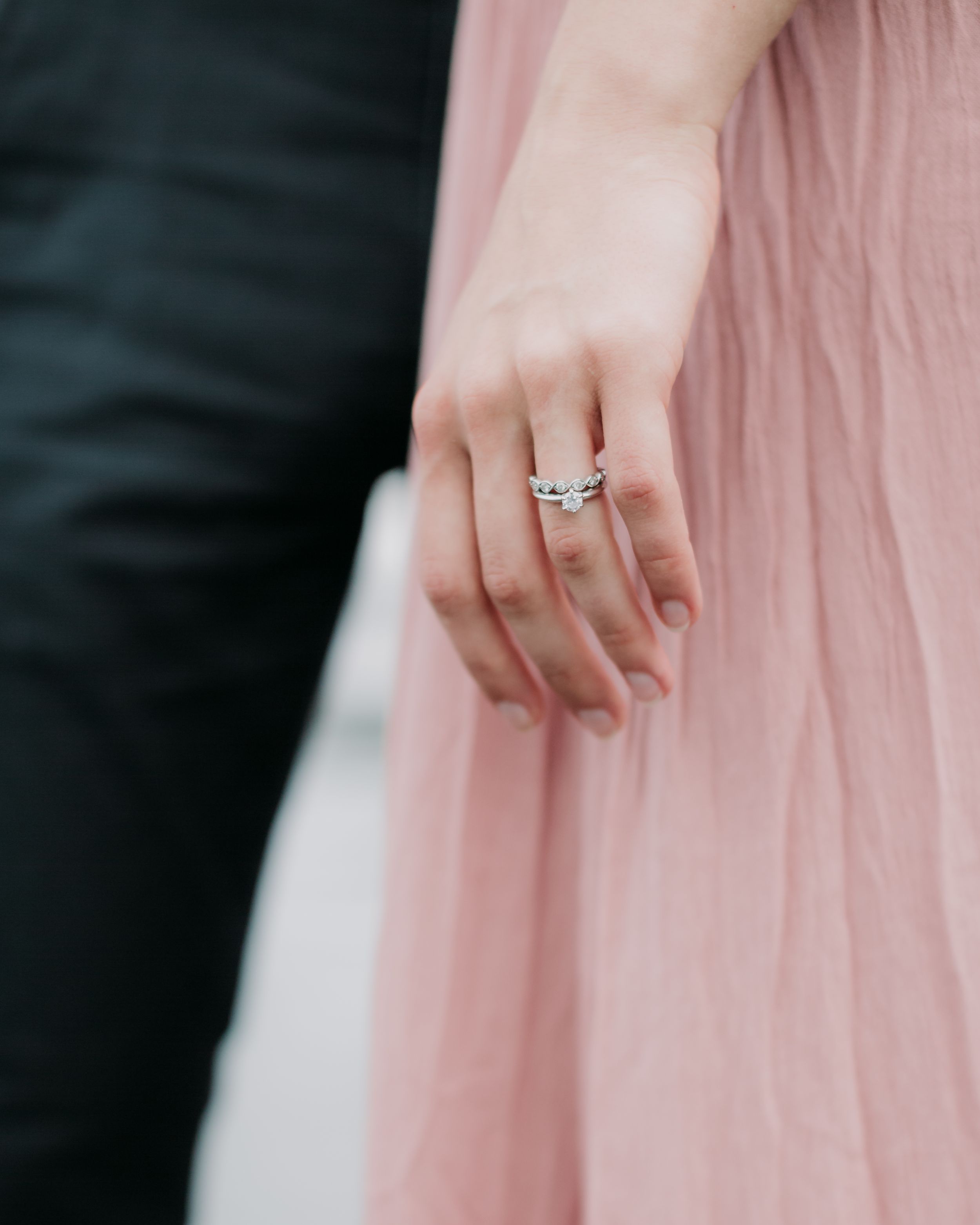 Close-up of engagement ring on woman's hand wearing pink dress against dark clothing.