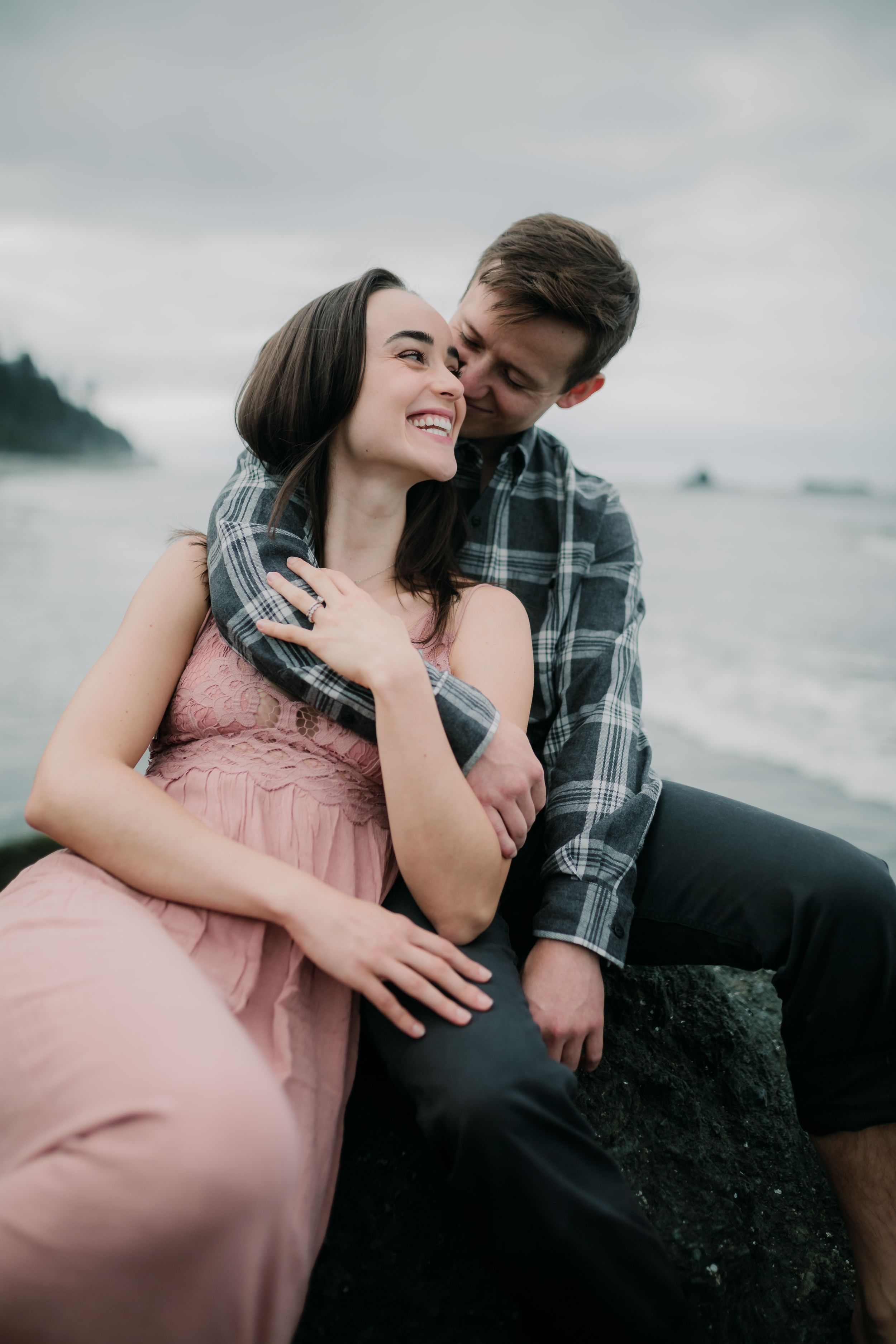 Couple sharing intimate moment while sitting on coastal rocks with ocean view.