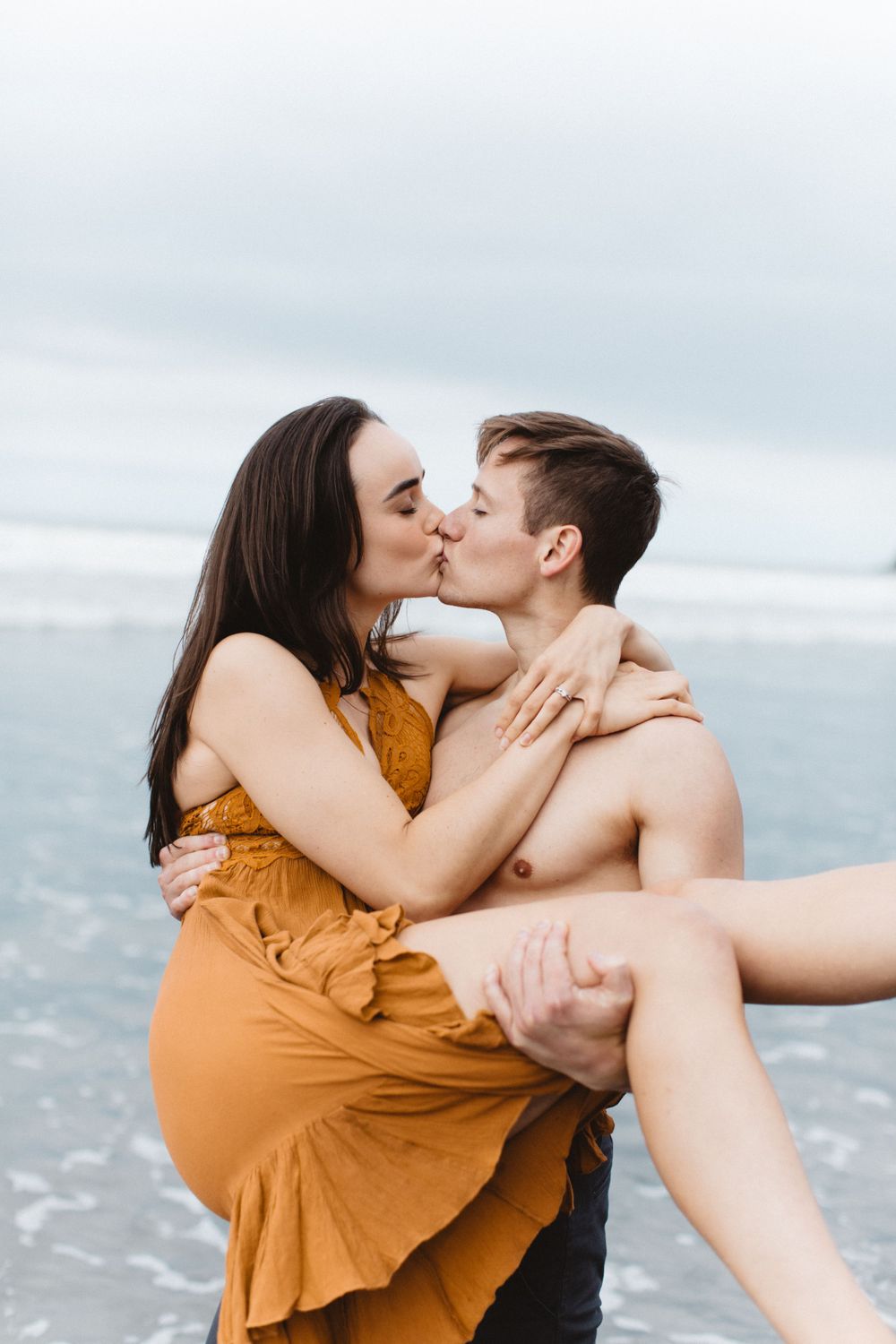 Intimate moment shared between couple on beach with ocean waves in background.