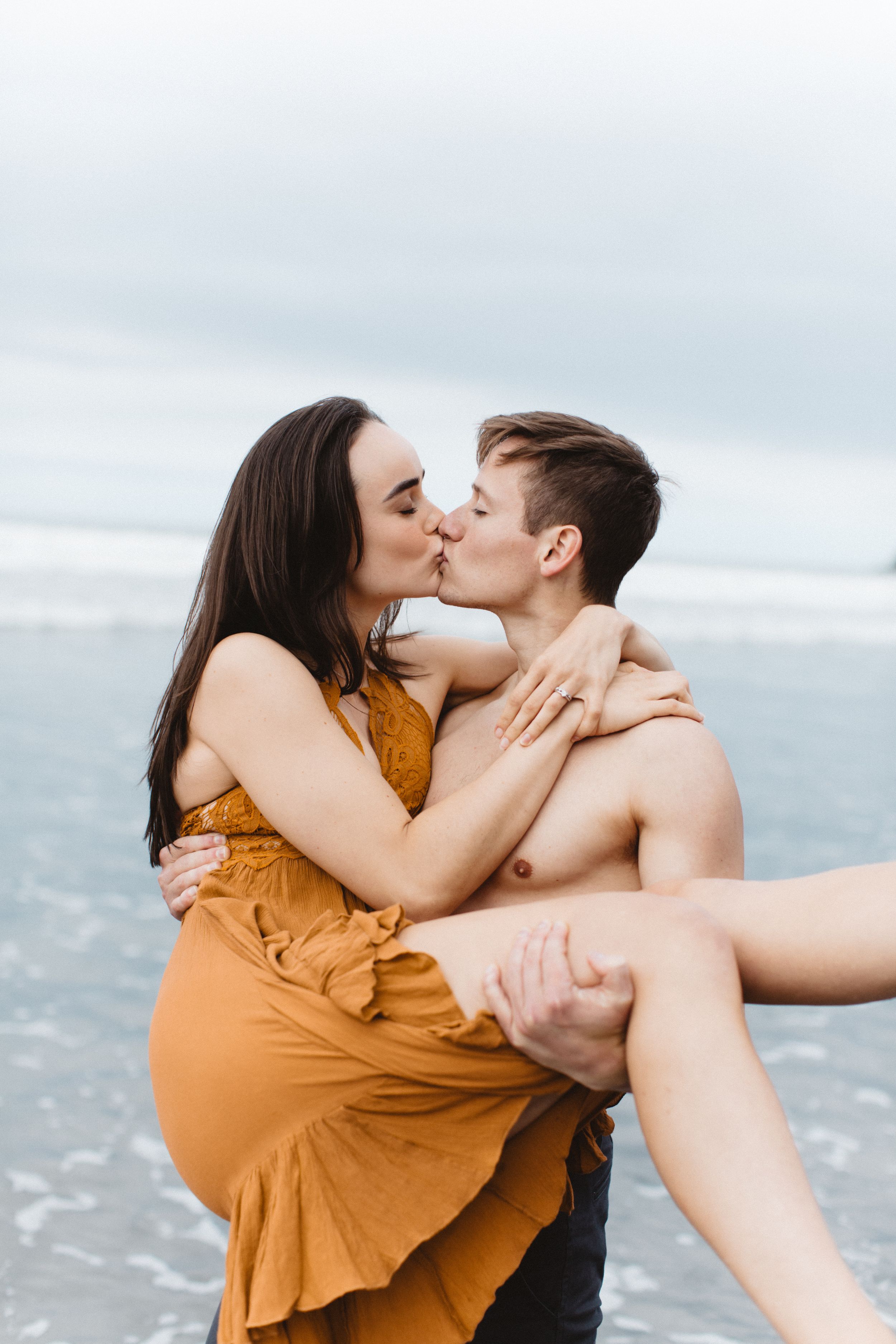 Intimate moment shared between couple on beach with ocean waves in background.