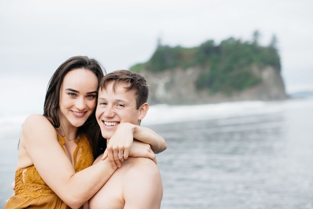 Happy couple embracing on beach with dramatic coastal cliffs in background.