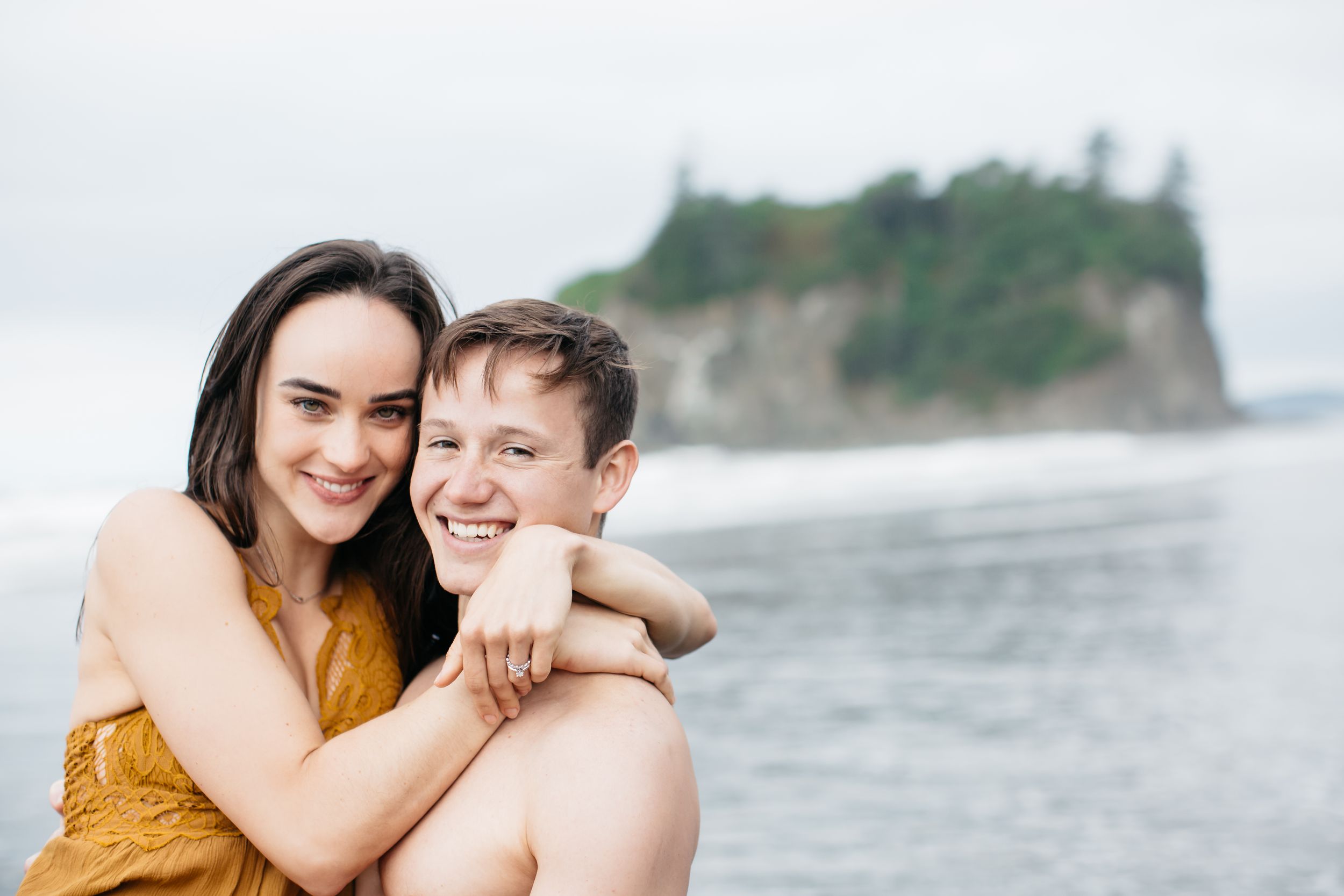 Happy couple embracing on beach with dramatic coastal cliffs in background.