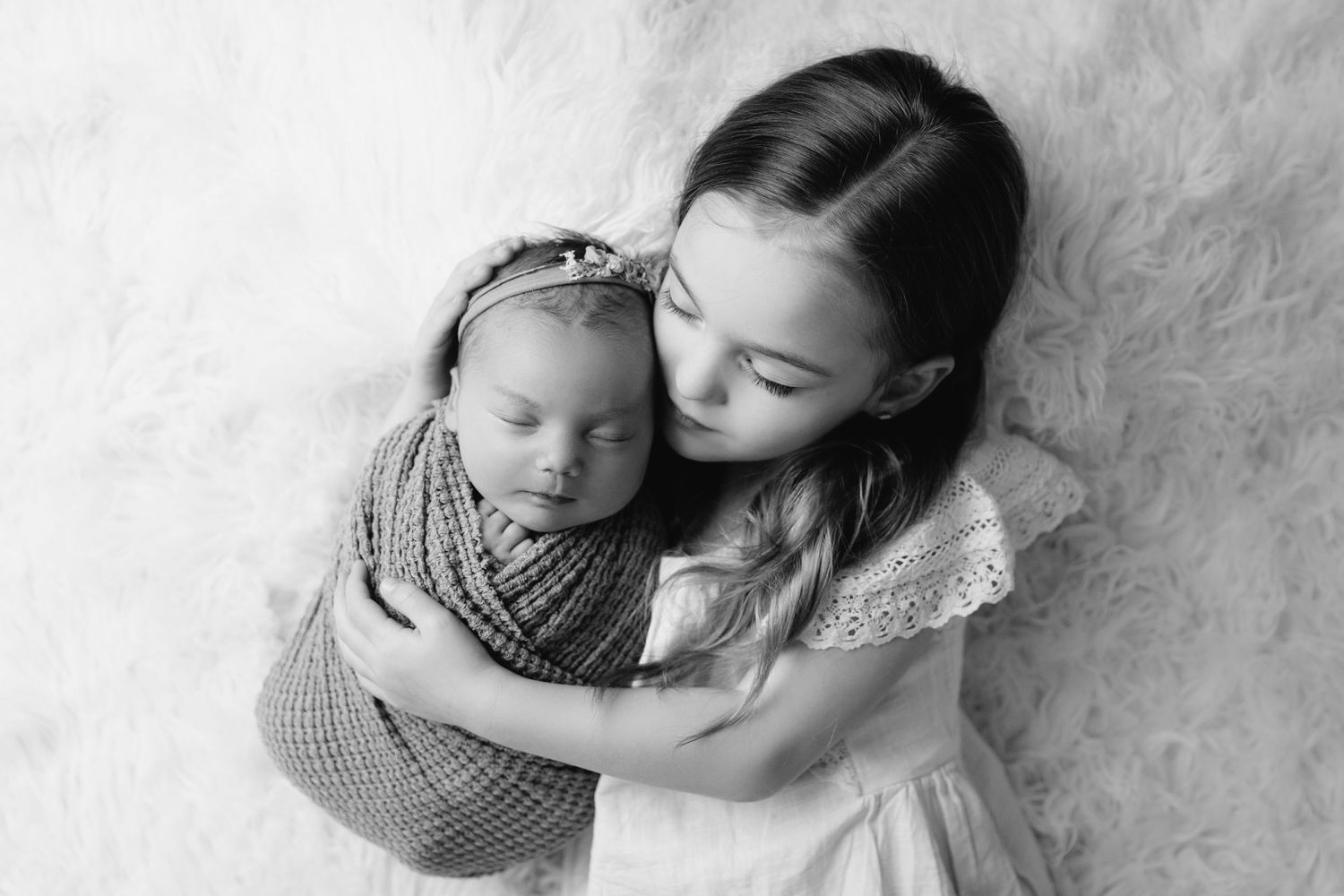 little girl cuddles her newborn baby sister during studio newborn photography session in Kansas City, MO