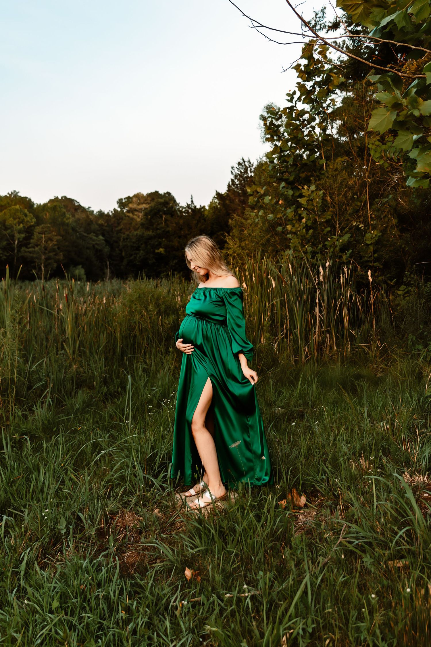 Woman in emerald green dress standing gracefully in a meadow during sunset.