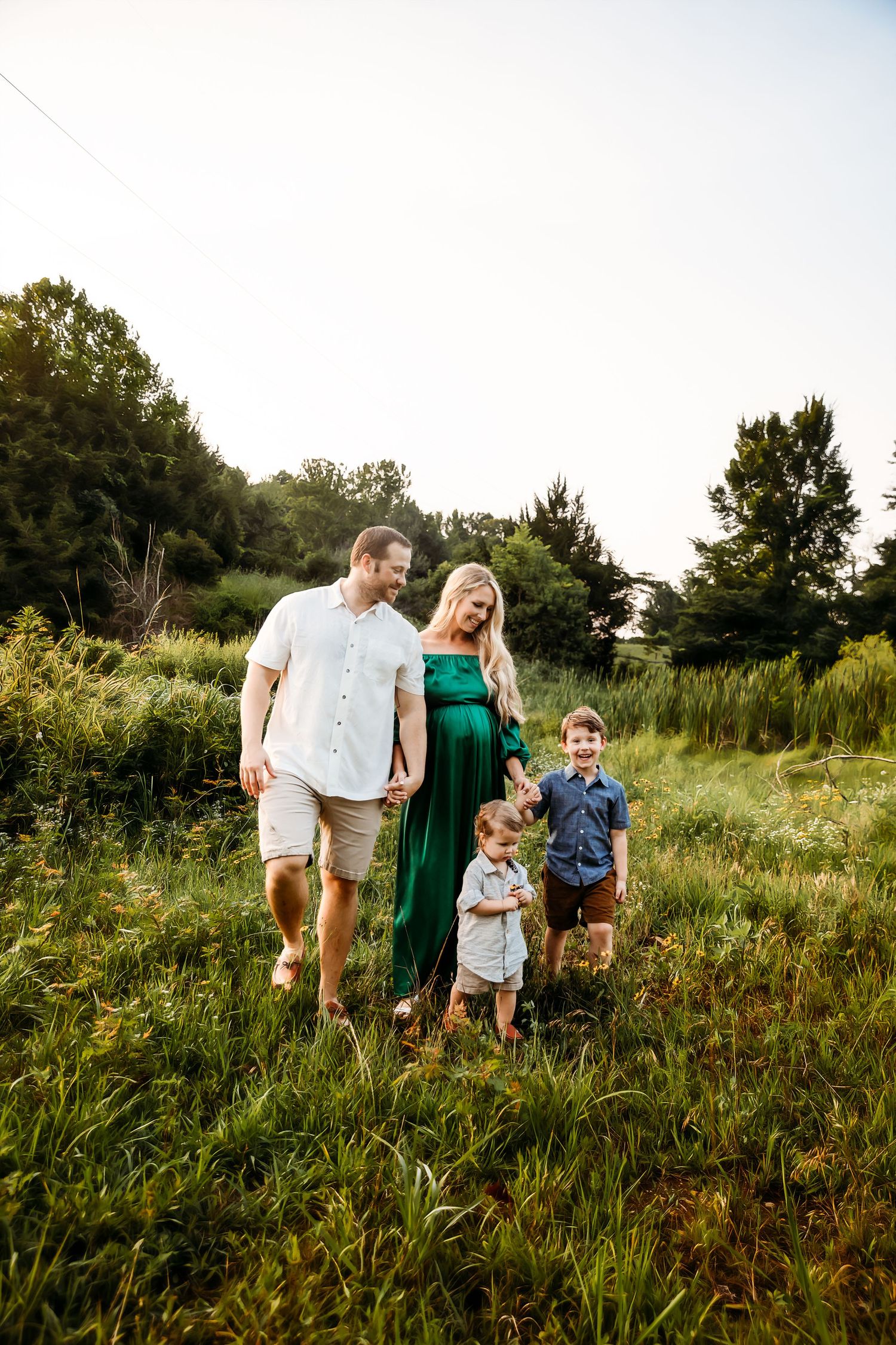 Family portrait in a lush green field during golden hour, wearing casual summer attire.