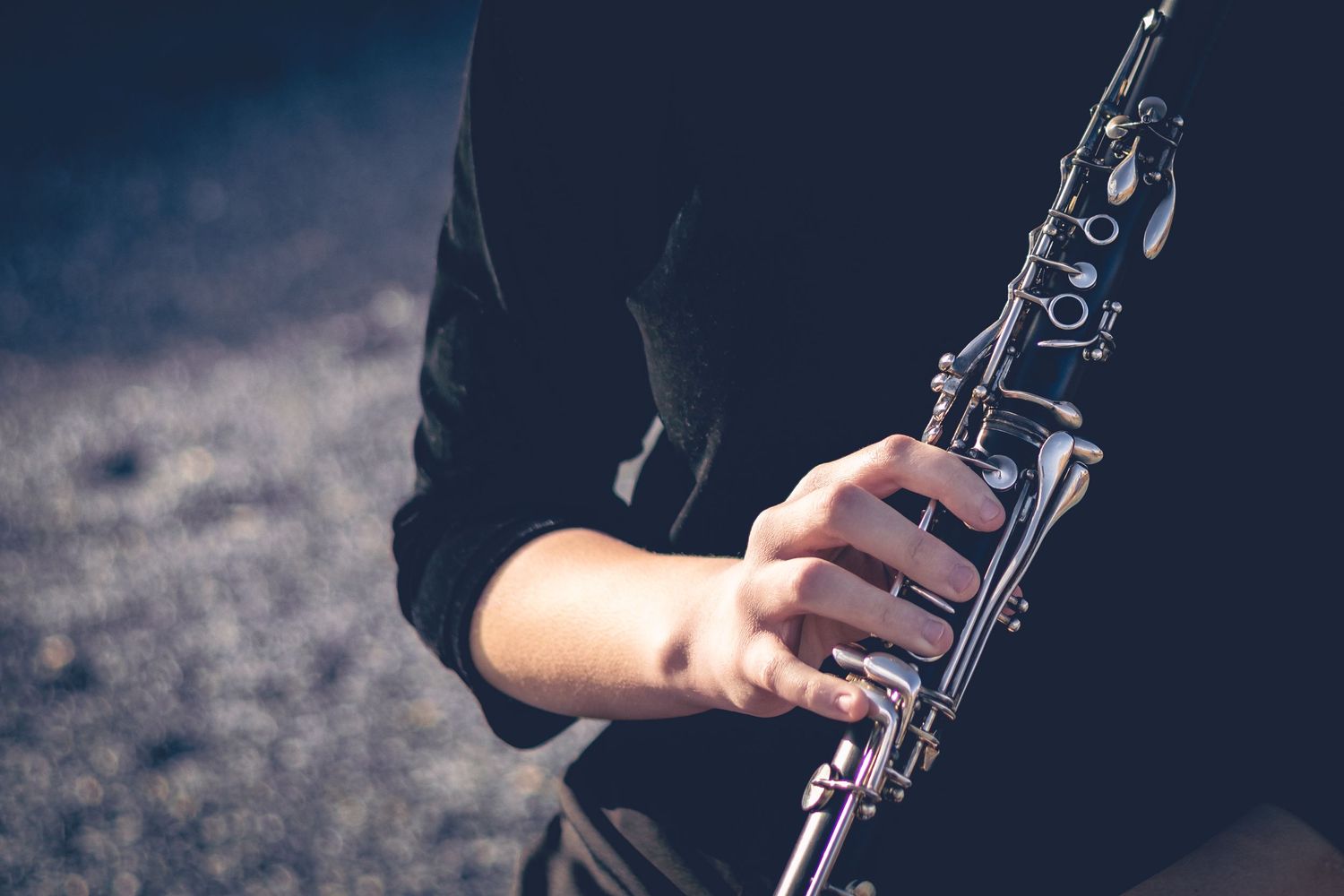 A person dressed in black plays a clarinet, holding it with both hands against an out-of-focus background.