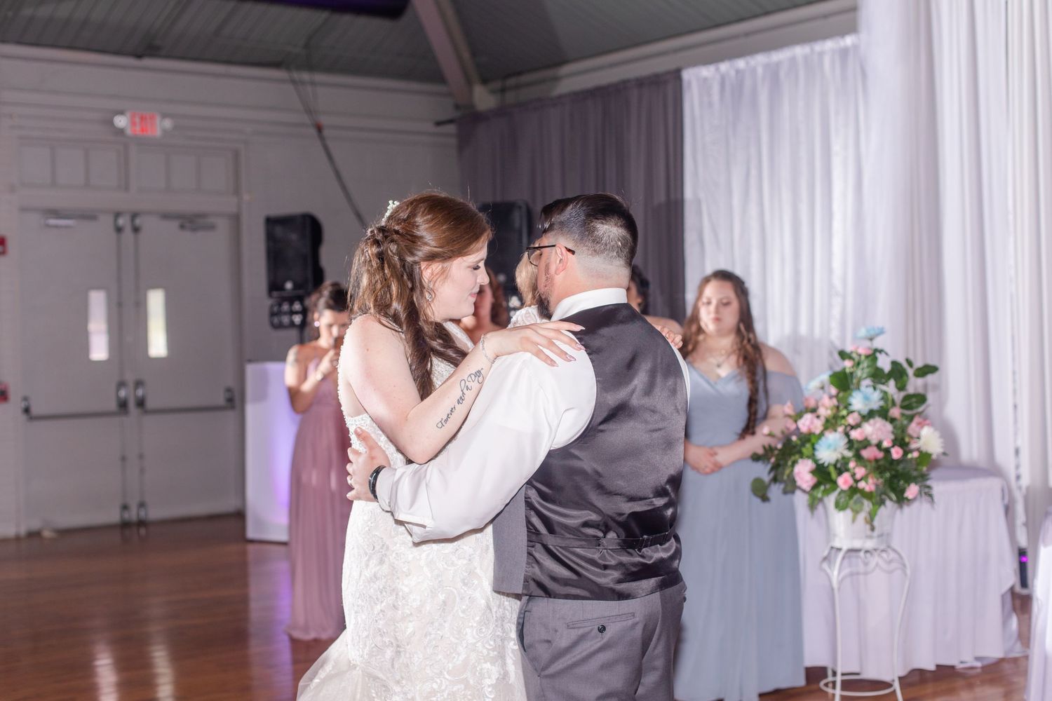 Wedding reception venue with industrial ceiling, white draping and purple accent lighting.