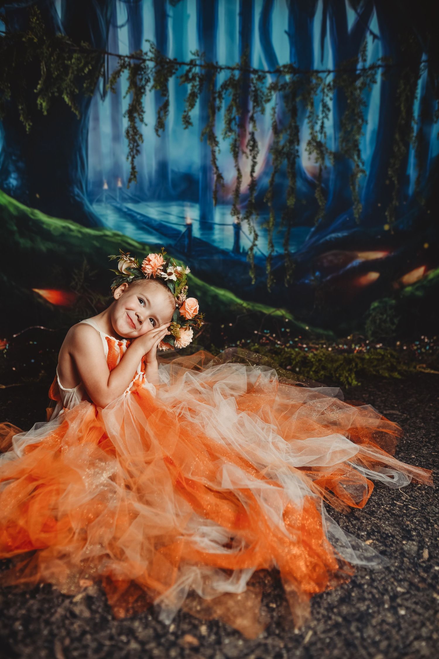 Person in flowing orange tulle dress poses dramatically in mystical blue-lit forest setting.