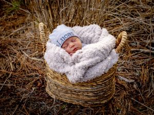 Newborn baby sleeping in a cozy woven basket wrapped in soft white blanket.
