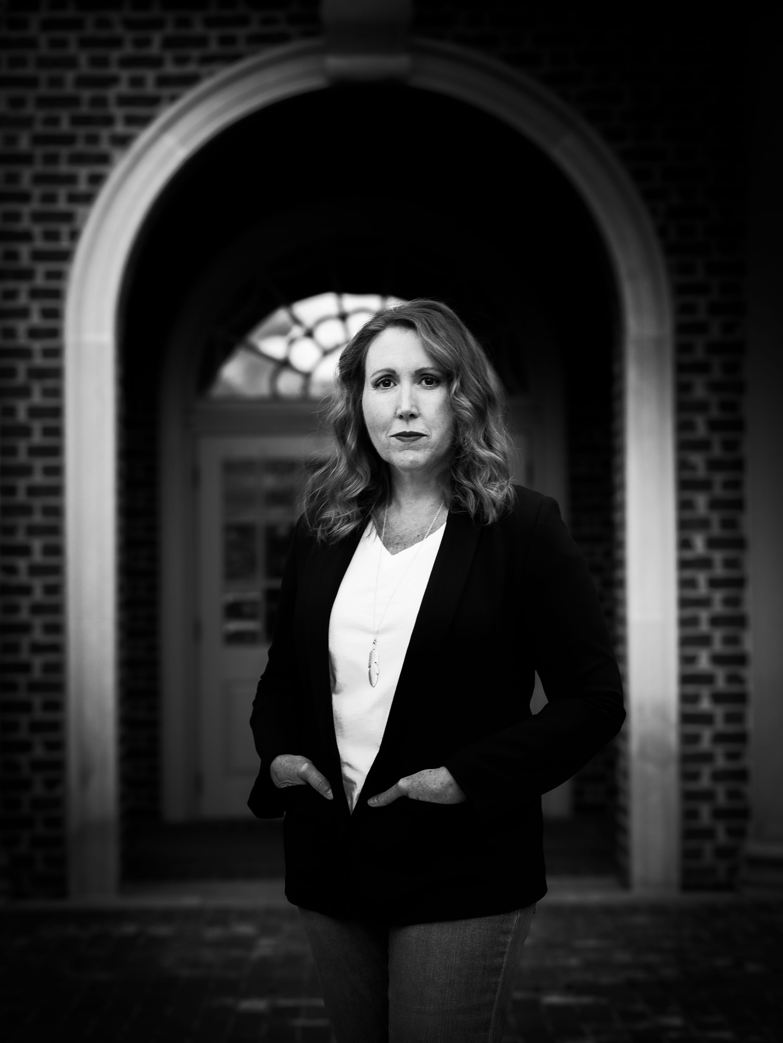 Professional portrait taken under a brick archway in black and white.