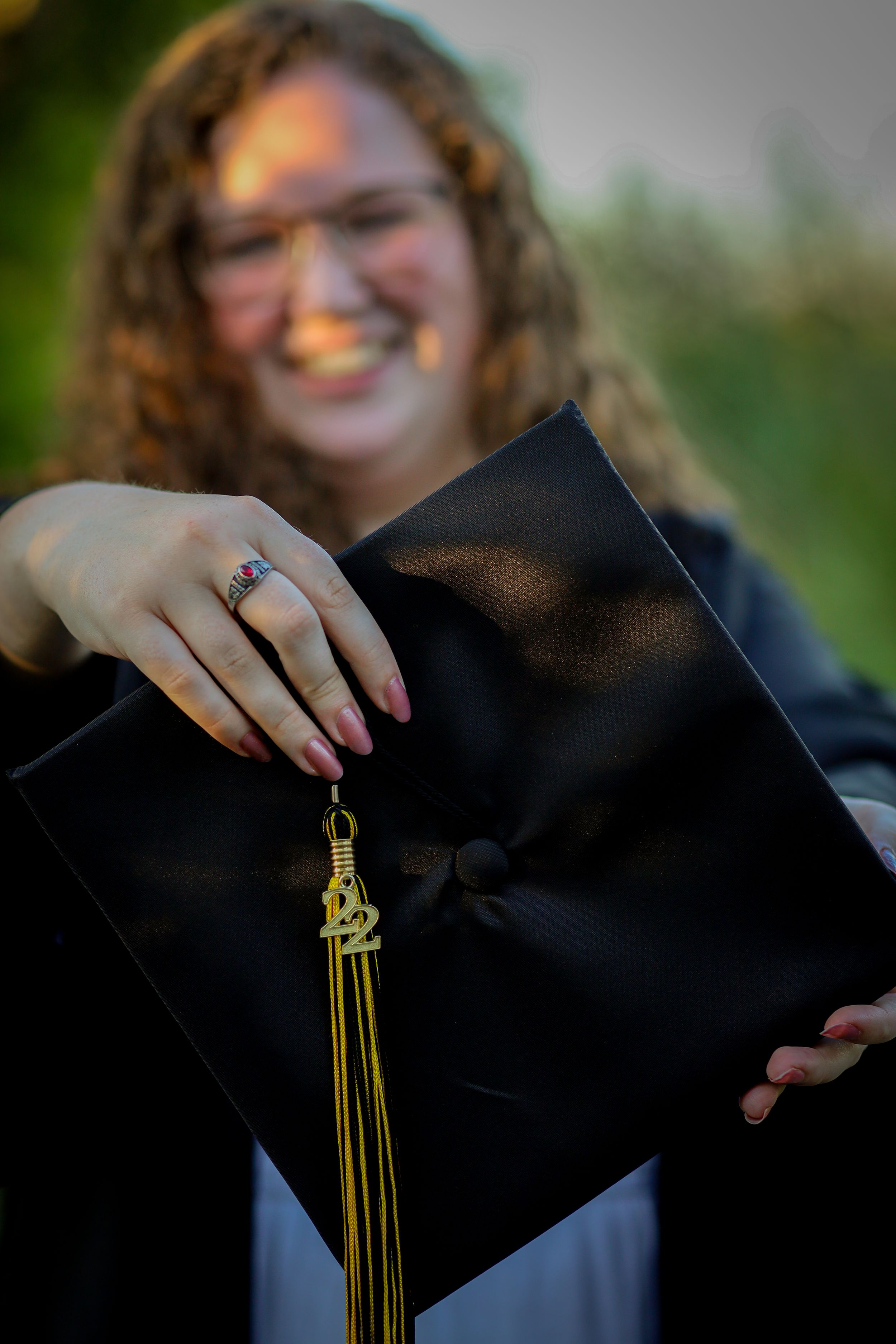 Graduate holding cap with yellow tassel against blurred outdoor background.