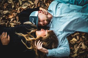 Two people lying on autumn leaves wearing casual clothing.