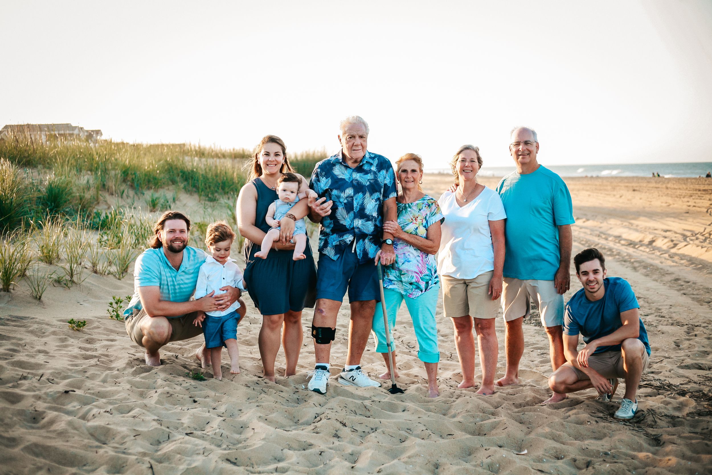 Family group wearing coordinated blue and white outfits posing on beach at sunset.