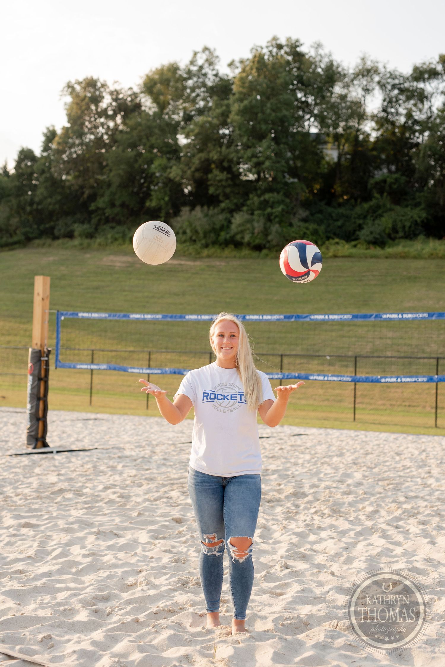 Volleyball player juggles two volleyballs on sandy court during practice session.