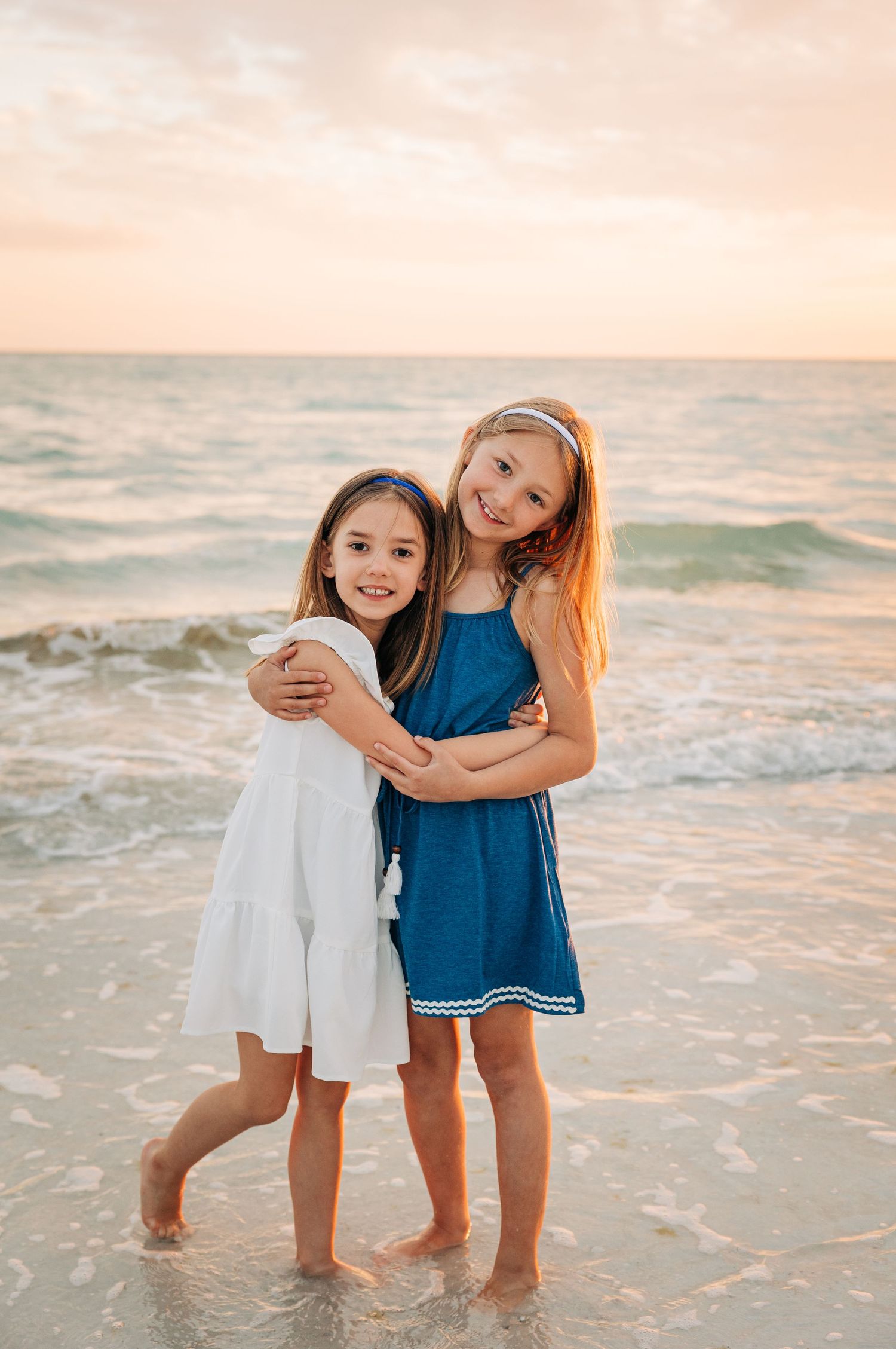 Two young sisters hug each other on Siesta Key Beach. Photographed by Sarasota Photographer Samantha Brown Artistry.