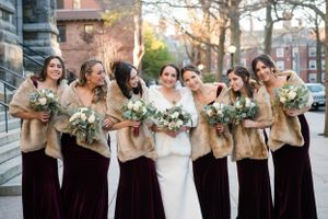 Bridal party in burgundy velvet dresses and tan shawls posing together outdoors.