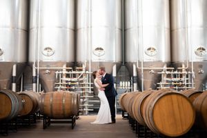 Wedding couple poses in elegant winery barrel room with dramatic lighting.