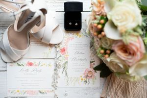 Wedding details including floral arrangements, invitations, and accessories on white rustic wood background.