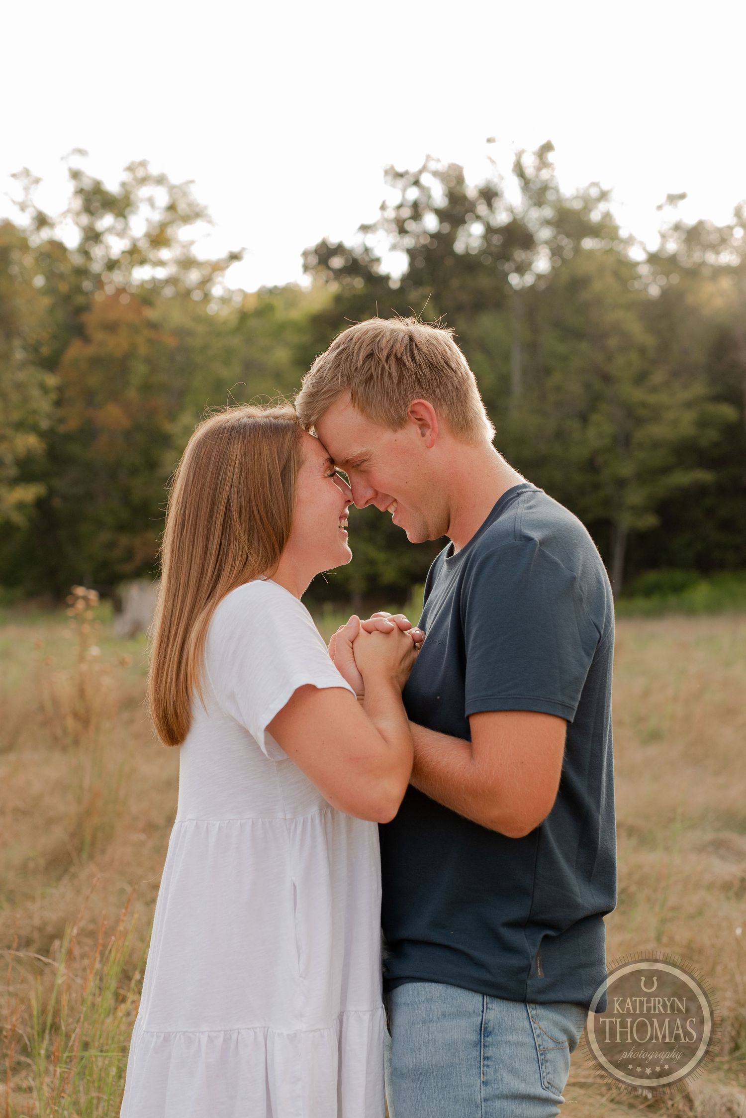 Couple shares intimate moment in tall grass during sunset photo session.