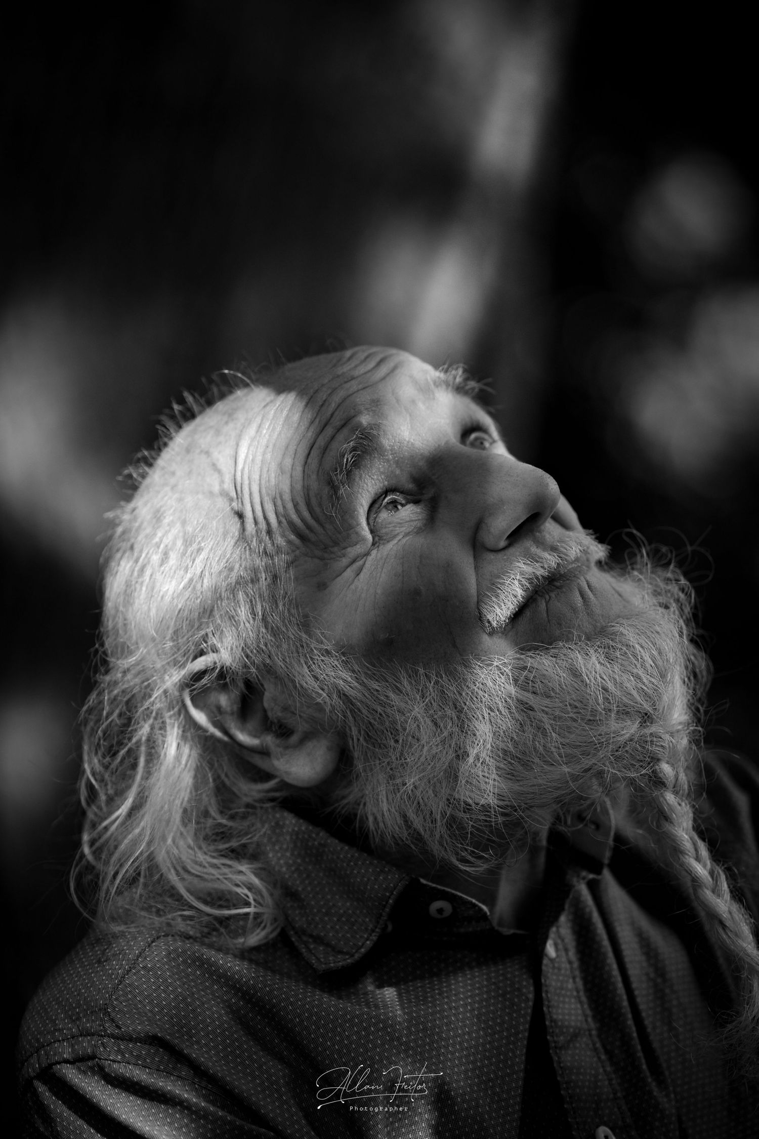 Black and white portrait of an elderly person with a long beard looking upward with a contemplative expression.