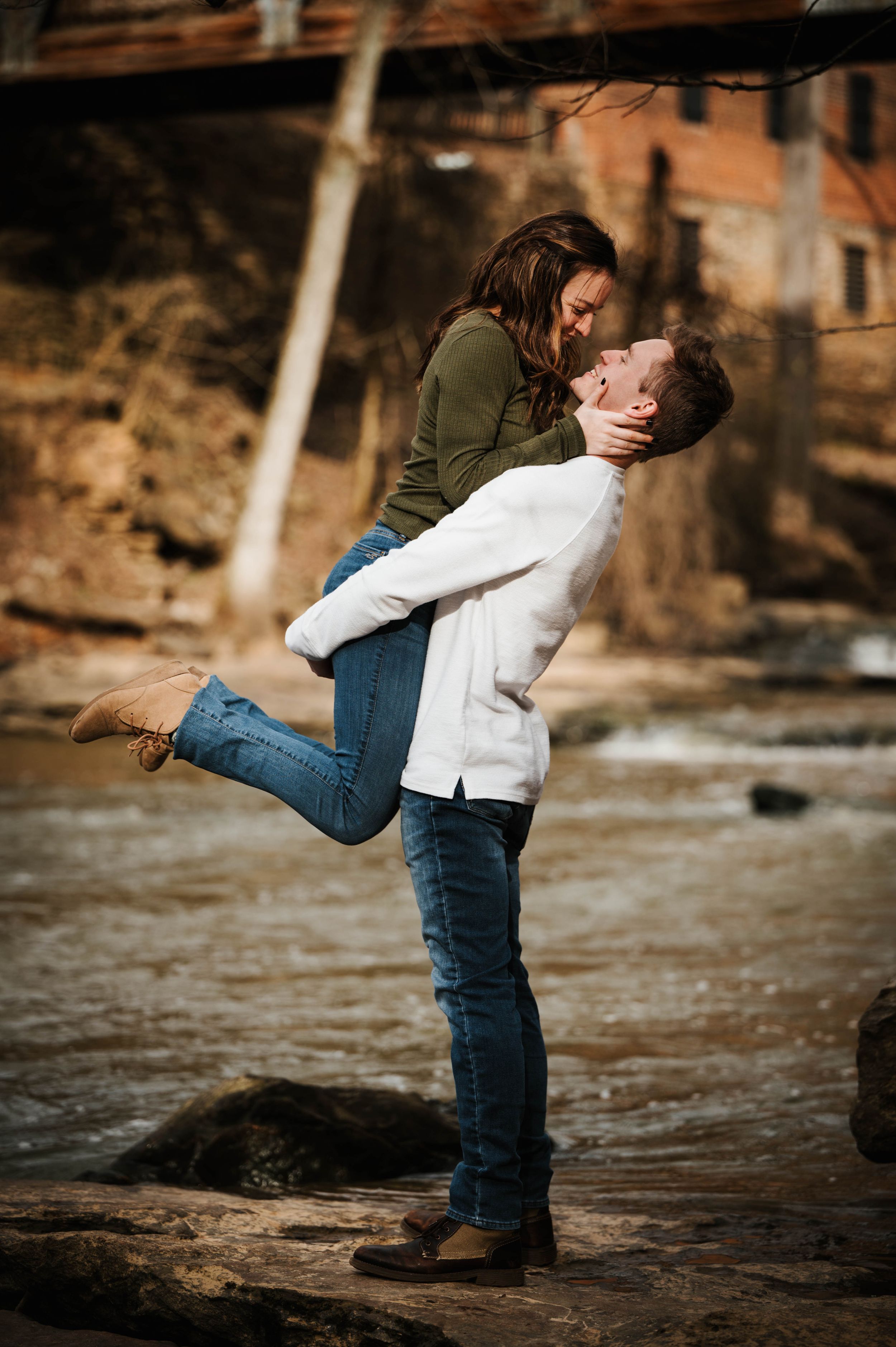 Romantic outdoor photoshoot showing playful embrace against rustic natural backdrop.