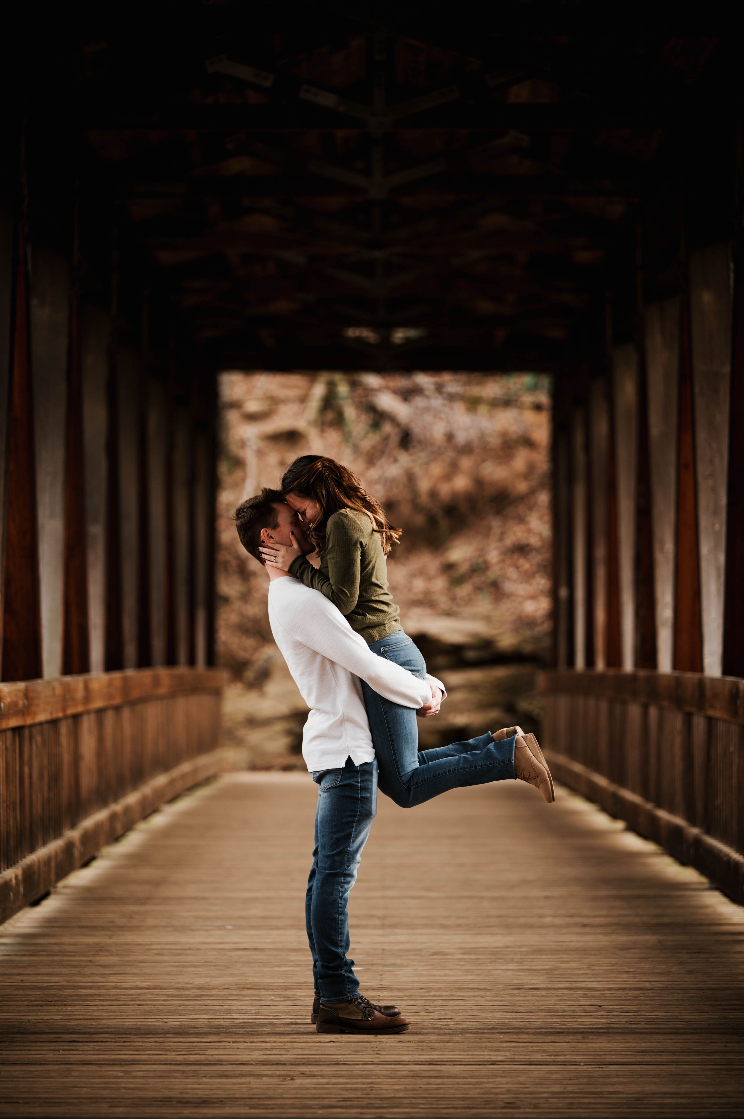 Romantic moment captured on wooden covered bridge with dramatic lighting.