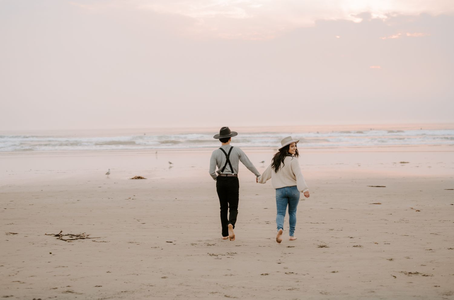 Couple holding hands while walking along a misty beach at sunset.