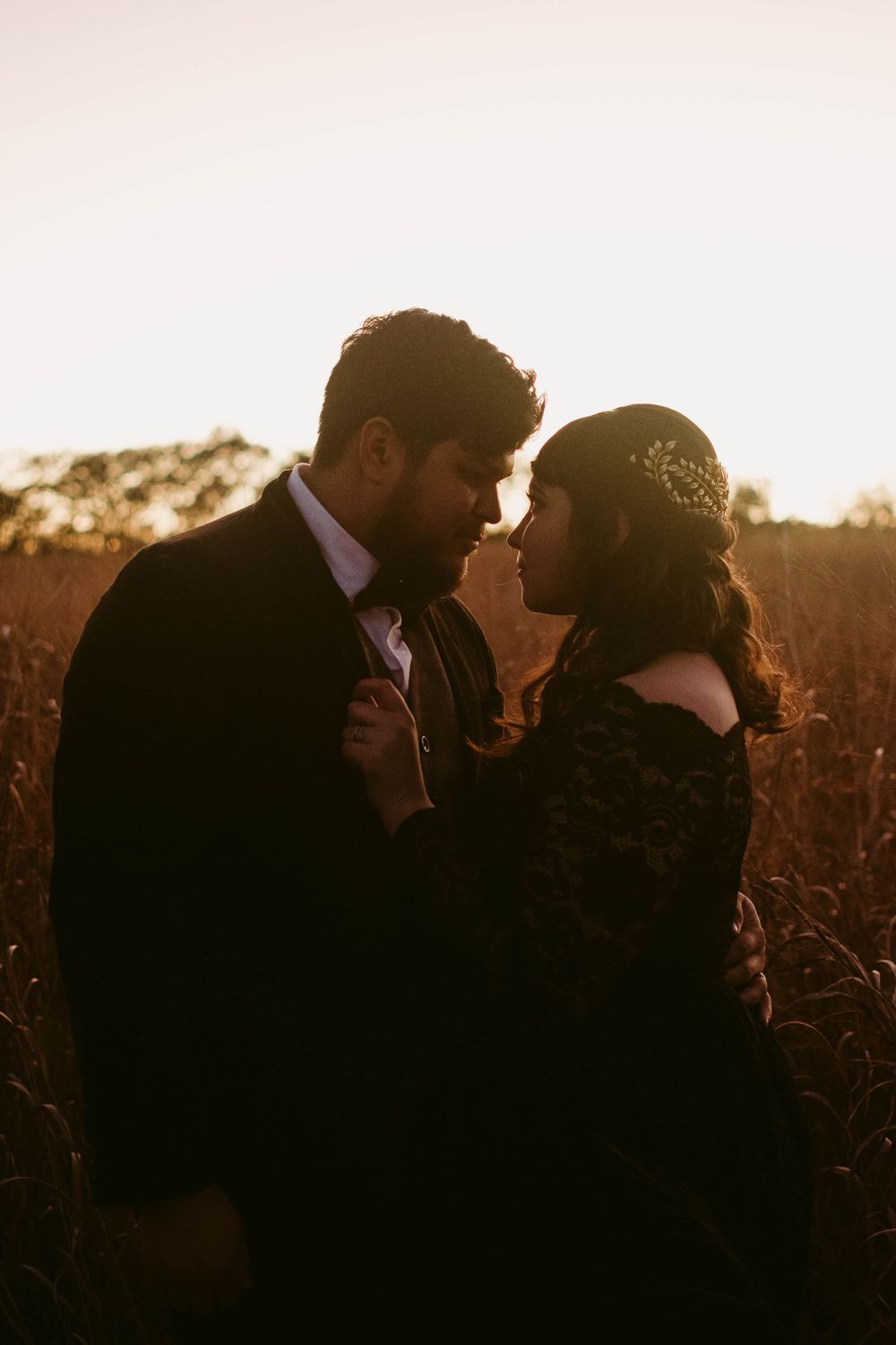 Romantic sunset silhouette of couple in formal attire embracing in golden field.