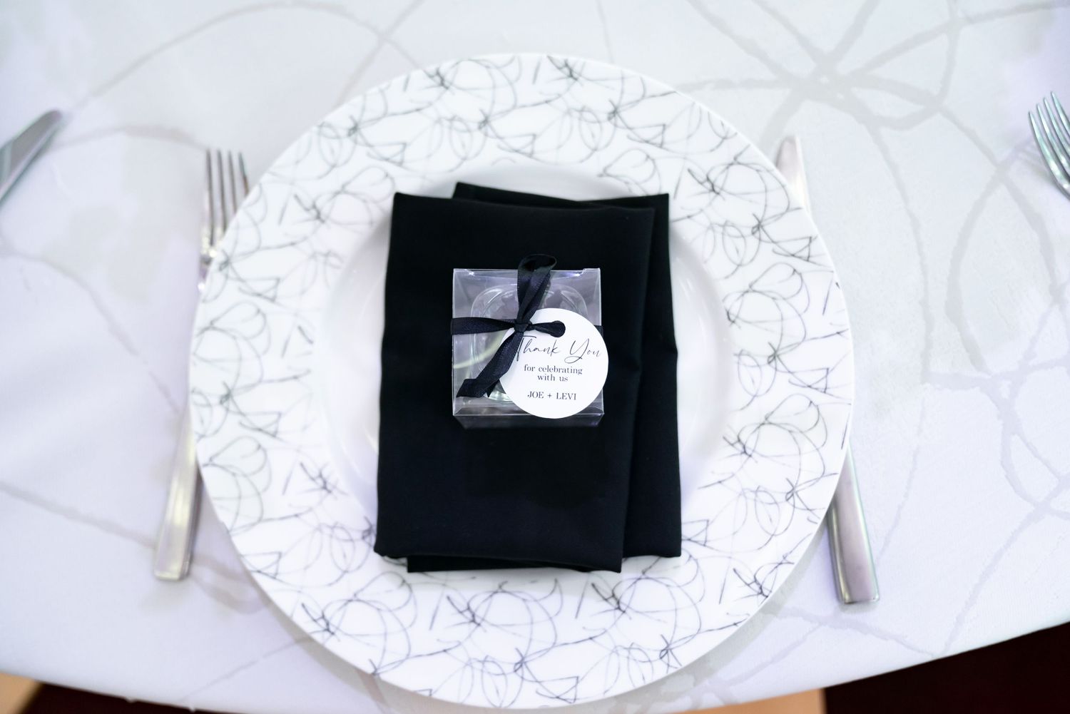 Place setting with black napkin and white patterned charger plate on wedding reception table.