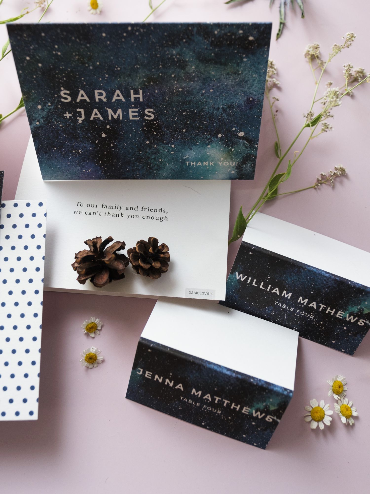 Wedding place cards and details with constellation-inspired designs on a pink background with small white flowers and pinecones.