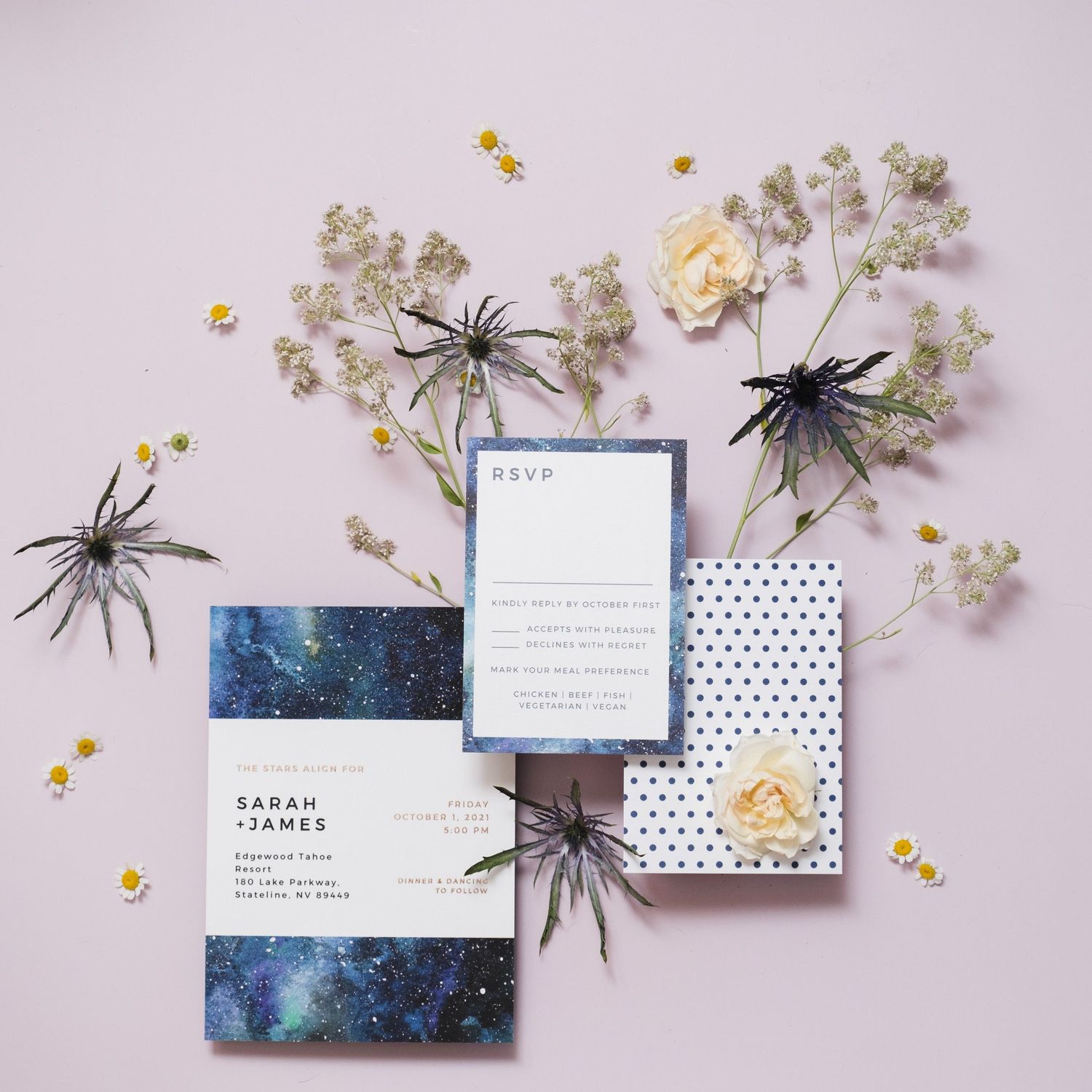Wedding invitation suite with dark blue galaxy pattern and small plastic spiders arranged with delicate baby's breath flowers.