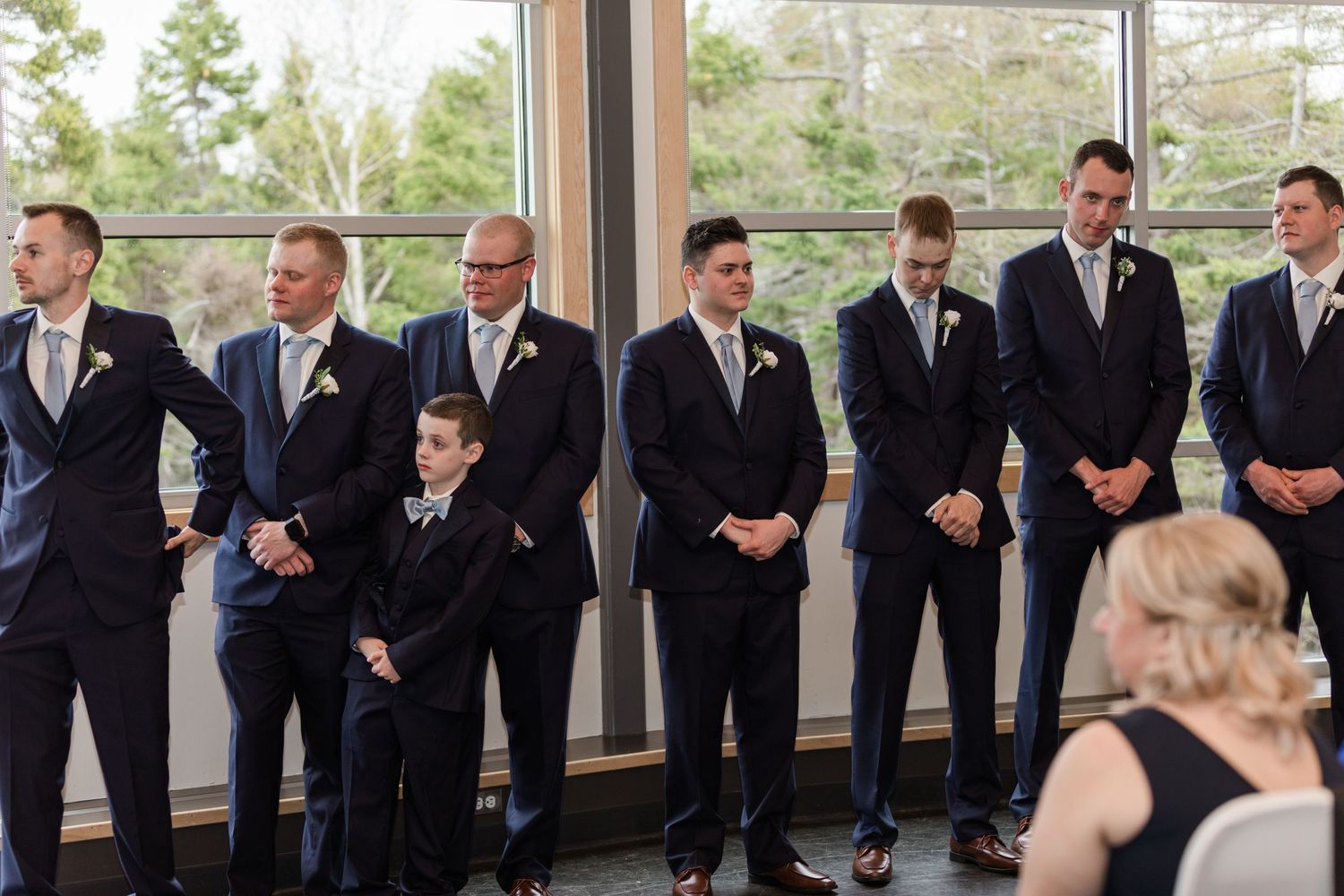 Groomsmen lined up in black suits against a bright window backdrop.