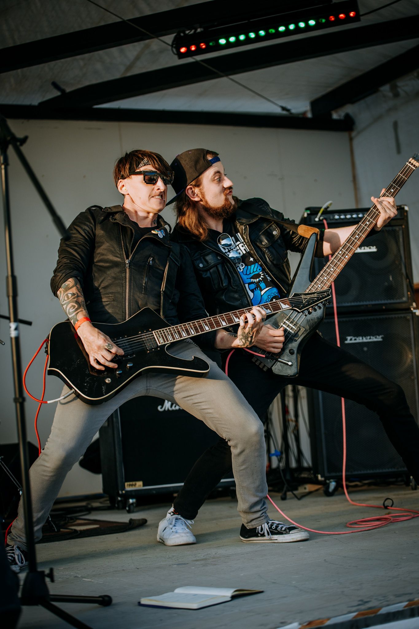Two guitarists perform in sync during high-energy rock performance with stage lighting.