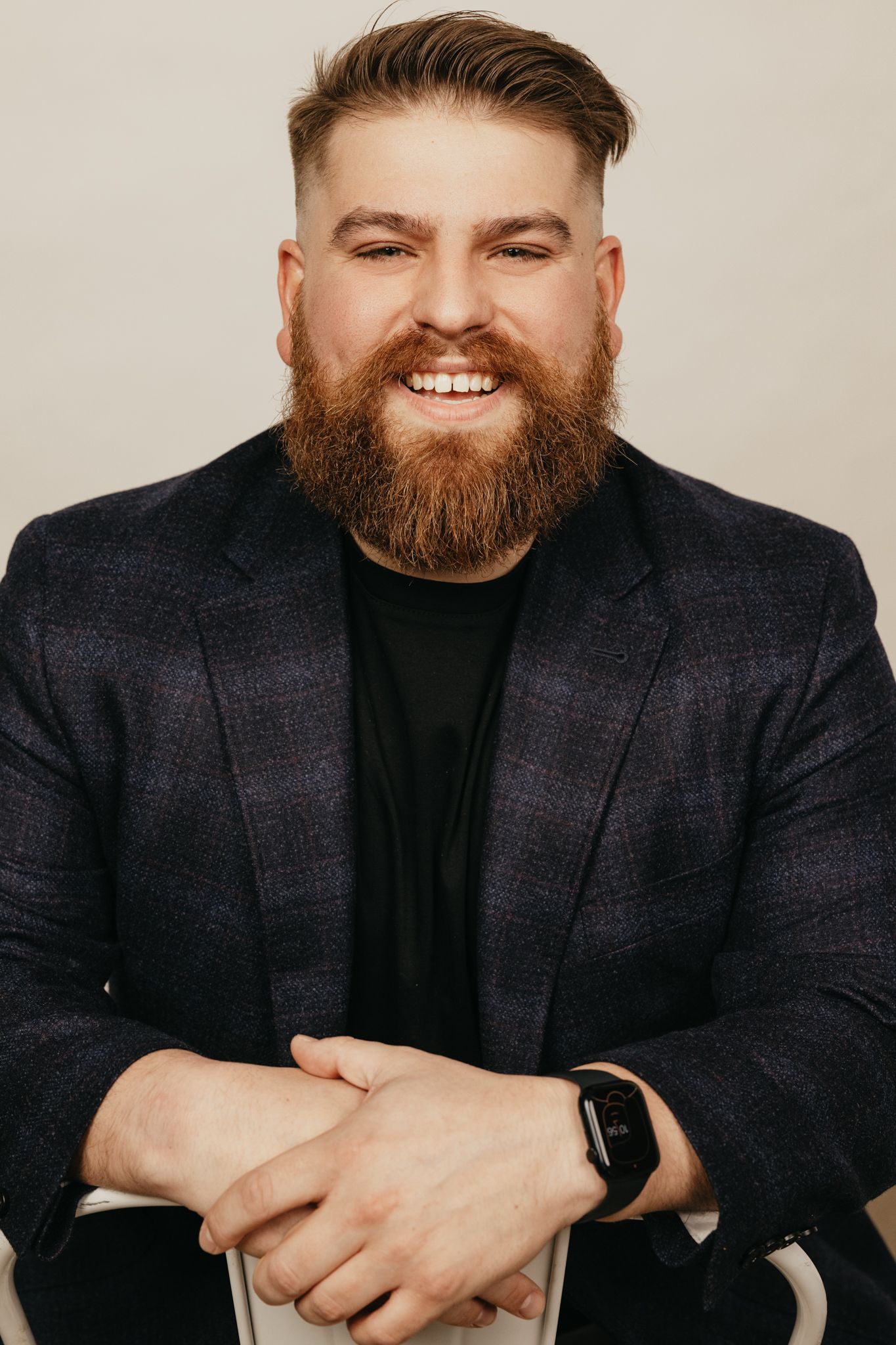 Professional studio portrait of a smiling person in a dark blazer wearing a smartwatch.