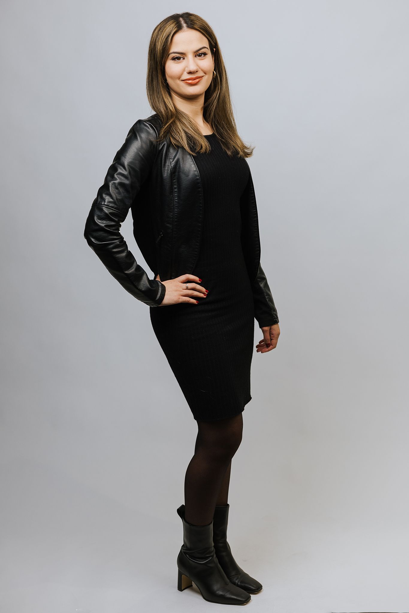 Professional studio portrait of woman in black leather jacket and dress against grey background.