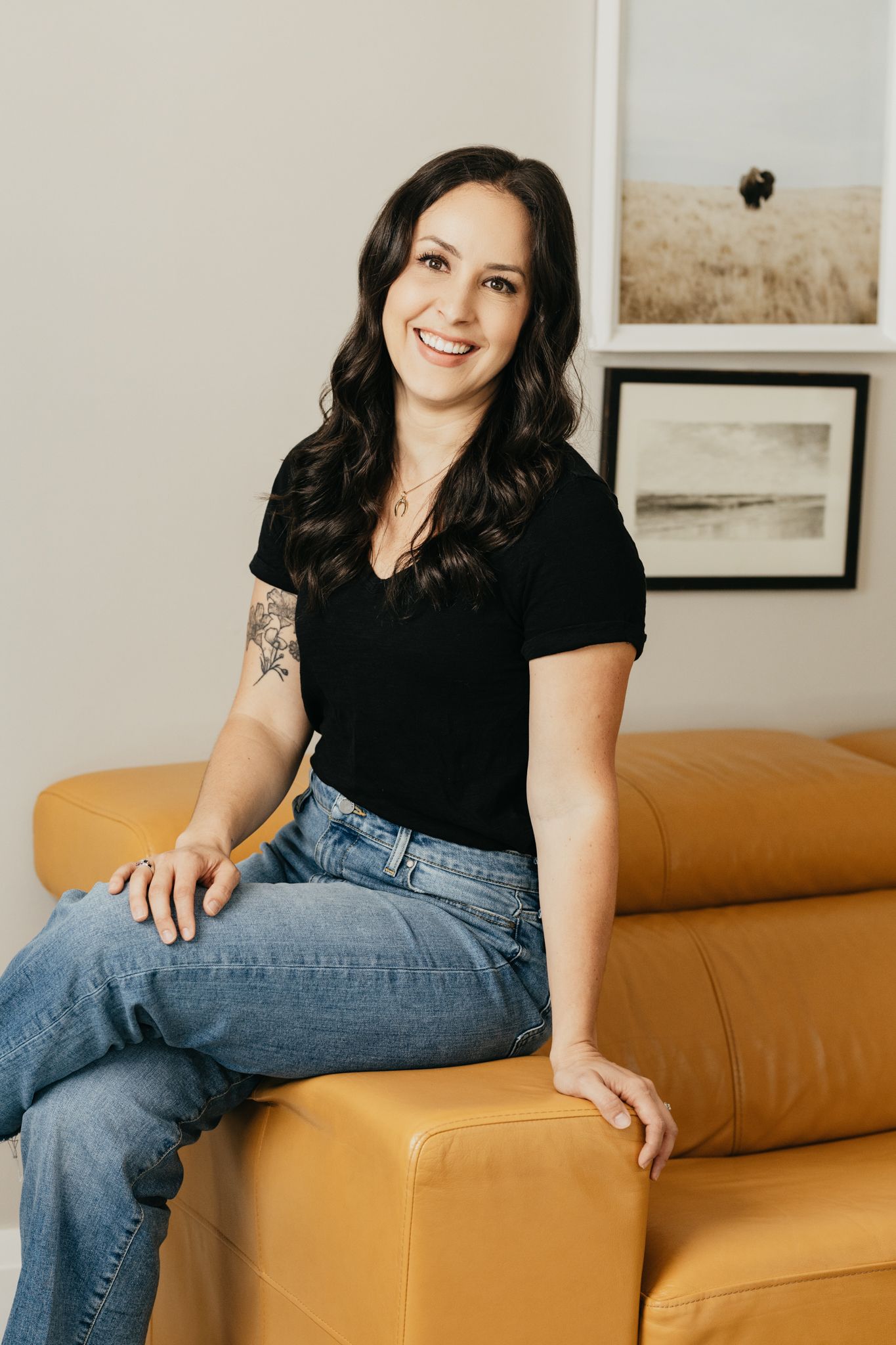 Professional portrait session on a tan leather couch showing casual relaxed poses in jeans and black top.